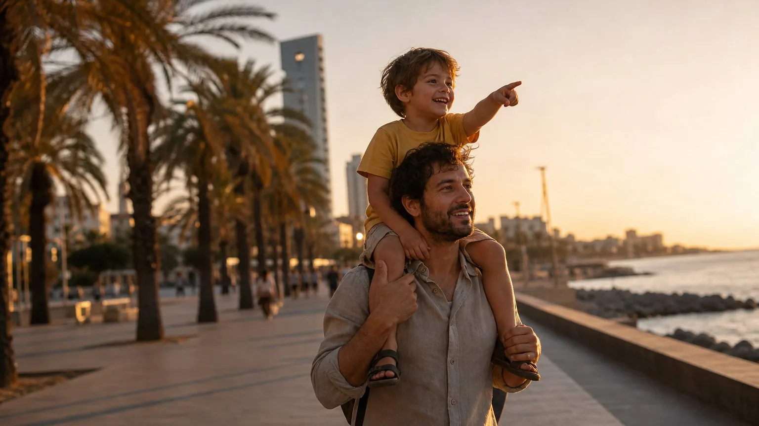 Child on a parent's shoulders along a Barcelona seafront promenade at golden hour