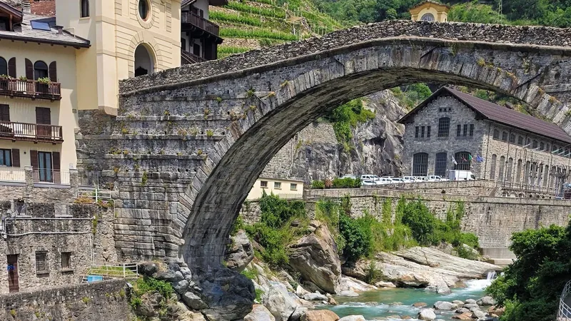 An old stone arch bridge spanning a rocky river below a hillside village.