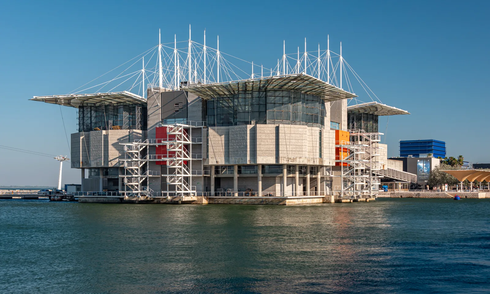 The Oceanário de Lisboa standing on pillars in the water of the Doca dos Olivais at Parque das Nações, under a clear sky