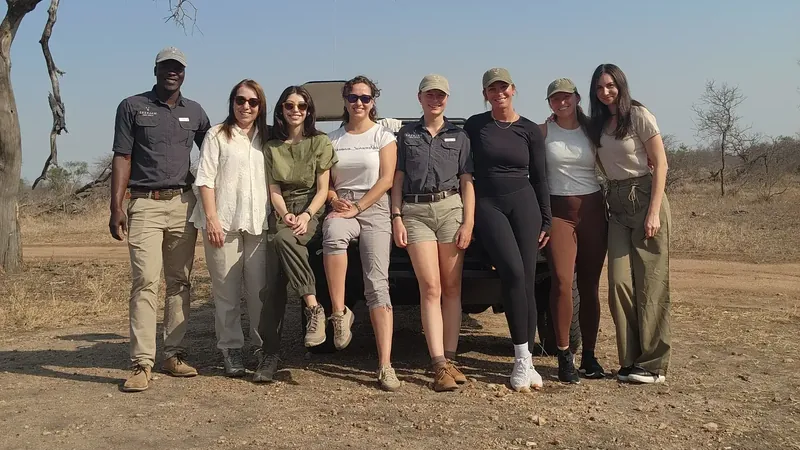 Eight travellers and a guide standing in front of a safari vehicle under a bare tree in South Africa's dry season