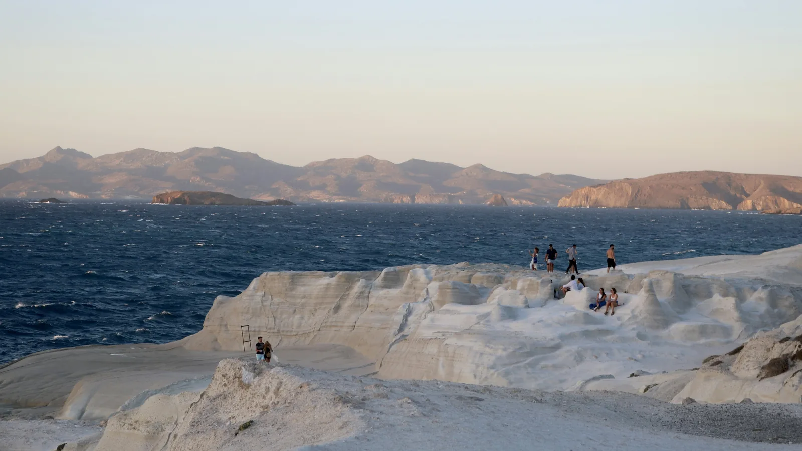 Visitors on the white rock shelf at Sarakiniko, Milos, at sunset
